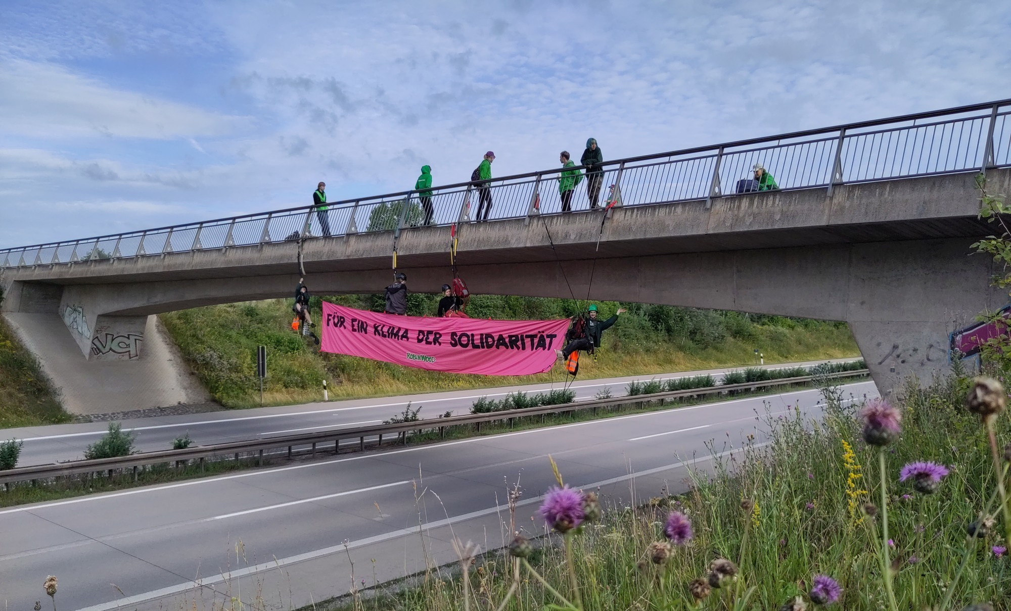 Kletternde mit rotem Protestbanner unter einer Brücke