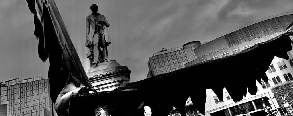 Schwarze Flügelschwingen des Ikarus-Vogels - Kunstaktion vor dem EU-Parlament gegen das Verfeuern der Wälder (Art Action & Foto: Comité Schone Lucht) Kunstaktion: Schwarze Flügelschwingen vor Gebäude