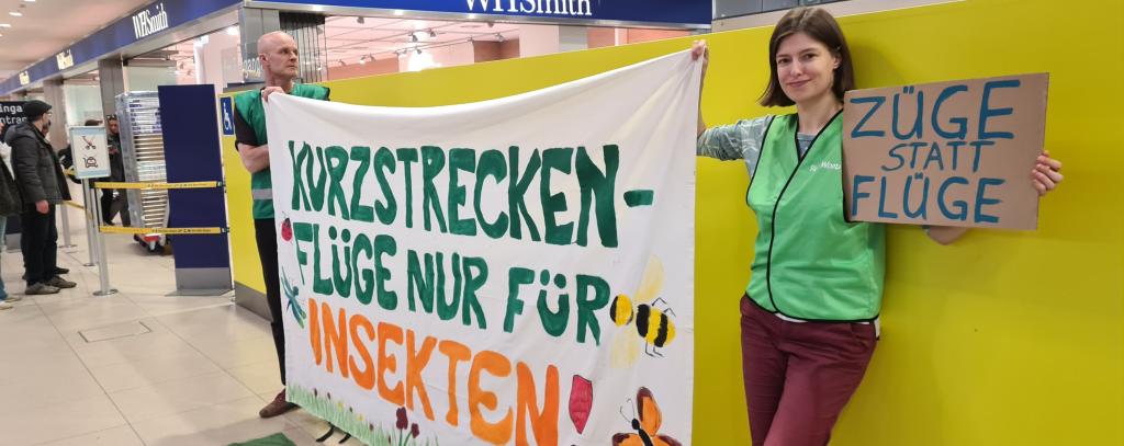 ROBIN WOOD-Protest am Flughafen Köln/Bonn für eine drastische Reduktion des klimaschädlichen Flugverkehrs Aktive mit Protestbanner "Kurzstreckenflüge nur für Insekten" in der Abflughalle eines Flughafens