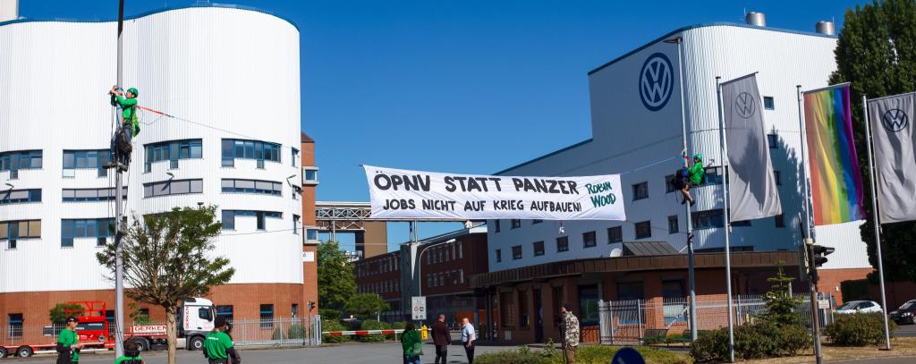 Protestbanner zwischen Laternenmasten vor VW-Werk: ÖPNV statt Panzer