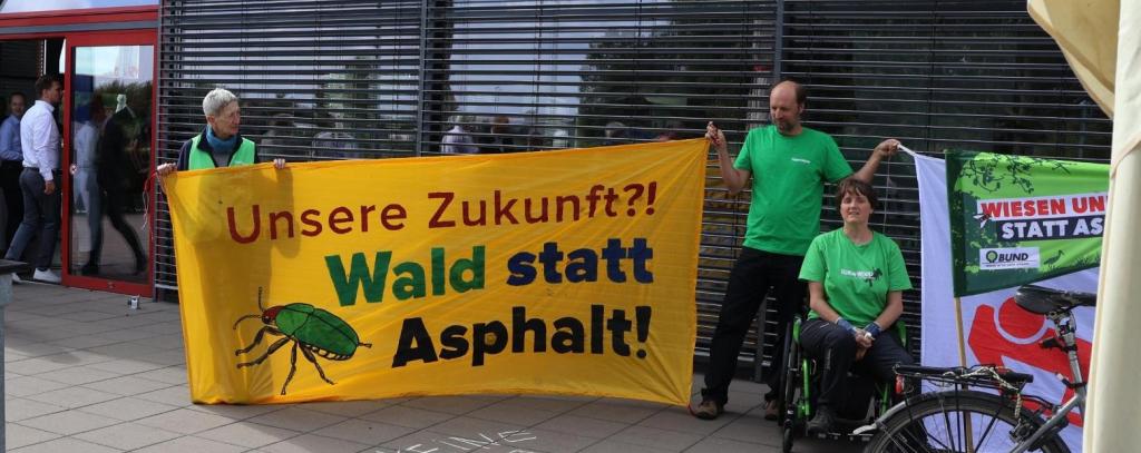 Umwelt-Protest gegen eine Pro-Autobahn39-Lobbyveranstaltung der Industrie- und Handelskammern, Isenbüttel, 08.07.2025 (Foto: ROBIN WOOD) Aktive mit gelbem Protestbanner gegen die A39 vor Gebäude