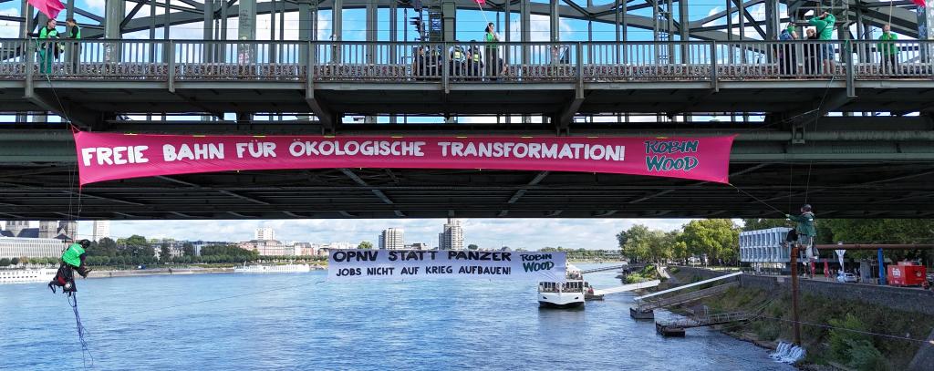Bannerprotest an der Hohenzollernbrücke in Köln: „Freie Bahn für ökologische Transformation!“ und „ÖPNV statt Panzer – Jobs nicht auf Krieg aufbauen" (Foto: ROBIN WOOD)