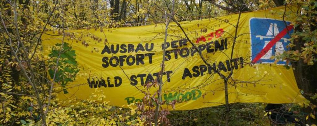 Gelbes Banner gegen Autobahnbau hängt im Wald