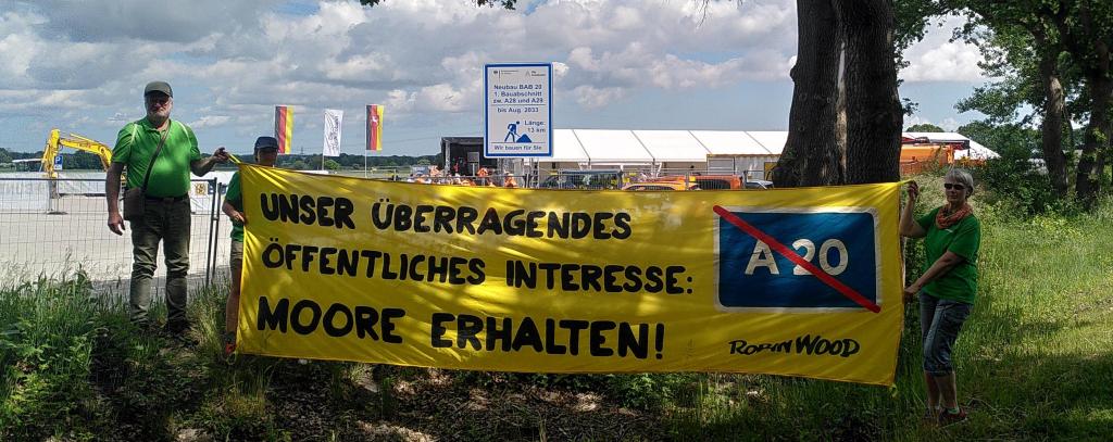 Menschen mit gelbem Protestbanner gegen die Autobahn A20 vor der Baustelle
