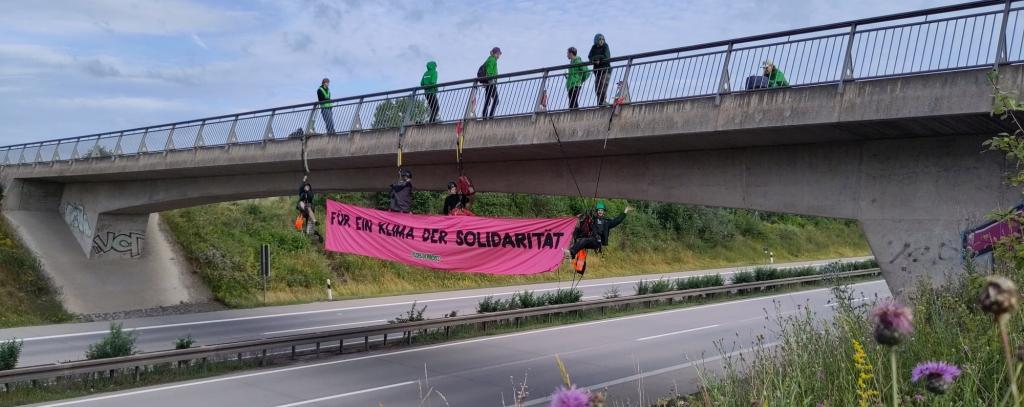 Aktive an einer Autobahnbrücke mit rotem Banner "Für ein Klima der Solidarität"