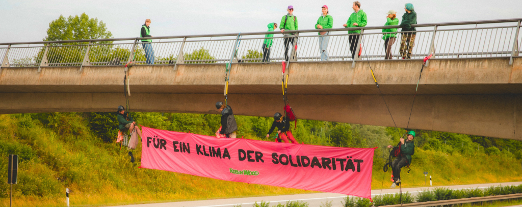 Rotes Banner unter Autobrücke und Aktive in grünen Pullovern auf der Brücke