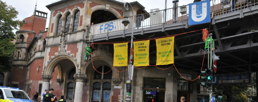 Drei gelbe Banner für die Verkehrswende unterhalb einer U-Bahnbrücke und zwei Kletteraktive