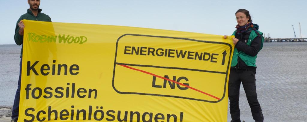 Bannerprotest anlässlich der Umweltministerkonferenz in Wilhelmshaven, 12.05.22 (Foto: ROBIN WOOD) Aktivist*innen mit einem gelben Banner gegen LNG, Aufschrift: Keine fossilen Scheinlösungen
