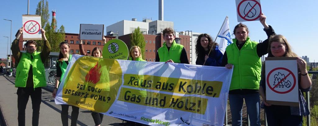 Protest gegen klimaschädliche Wärmeproduktion von Vattenfall vor dem Kraftwerk Moabit in Berlin (Foto: Ute Bertrand / ROBIN WOOD) Klimaschützer*innen mit Protestbanner "Raus aus Kohle, Gas und Holz!"