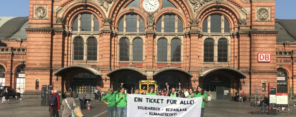 Für ein solidarisches Klimaticket und gegen die Verteuerung des Deutschland-Tickets – ROBIN WOOD-Aktive sind diese Woche überall im Bundesgebiet mit Protestschildern und -bannern unterwegs – auch vor dem Bremer Hauptbahnhof Gruppe mit Banner mit Aufschrift "Ein Ticket für alle" vor Bremer Hauptbahnhof