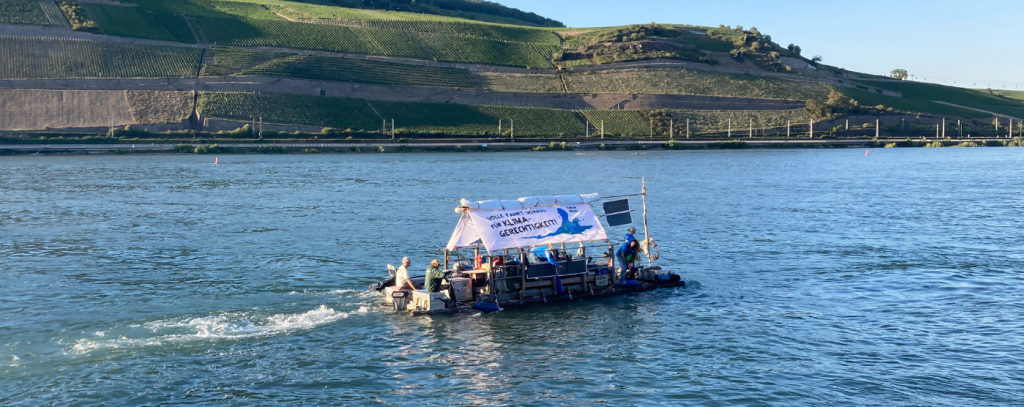 ROBIN WOOD-Floß für Klimagerechtigkeit auf der Fahrt nach Bingen (Foto: ROBIN WOOD) ROBIN WOOD-Floß auf dem Rhein vor Weinbergen