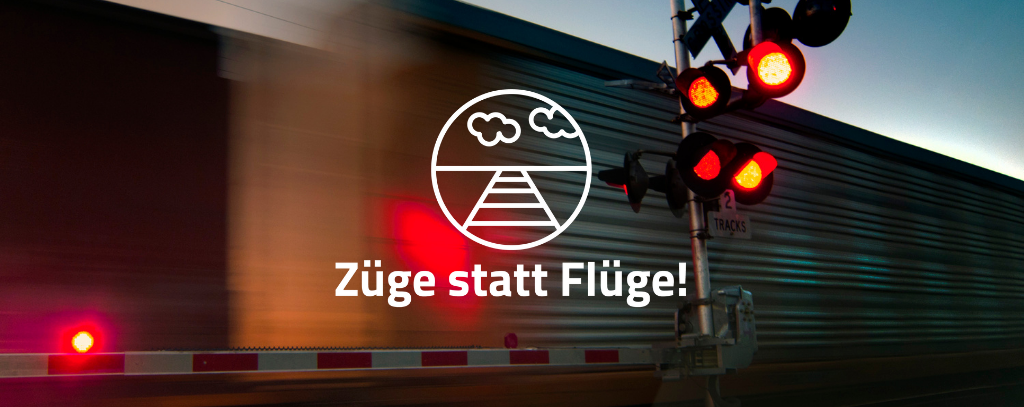 Robert Couse-Baker Das Bild zeigt einen Bahnübergang mit einer roten Ampel. Hinter der Ampel fährt ein Guterzug vorbei. Auf dem Bild ist das Kampagnenlogo und der Slogan "Züge statt Flüge" in weißer Schrift zu sehen.