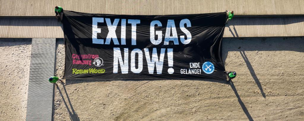 Protest gegen LNG auf Rügen. Dort ging dieses Jahr ein LNG-Terminal in Betrieb, das hoch umstritten ist und bislang kaum zur Energieversorgung beiträgt. (ROBIN WOOD / Daniel Müller) Banner mit Aufschrift "Exit Gas Now" auf dem Boden liegend