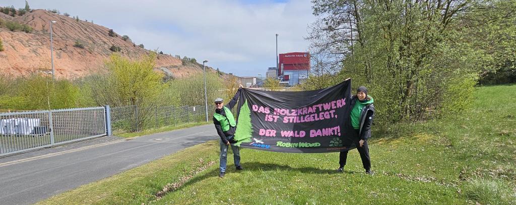 Zwei Aktive mit Protstbanner, dahinter ein Kraftwerk