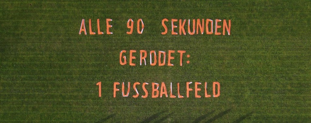 Luftaufnahme von einem Banner gegen Waldzerstörung,das auf einem Fußballfeld liegt