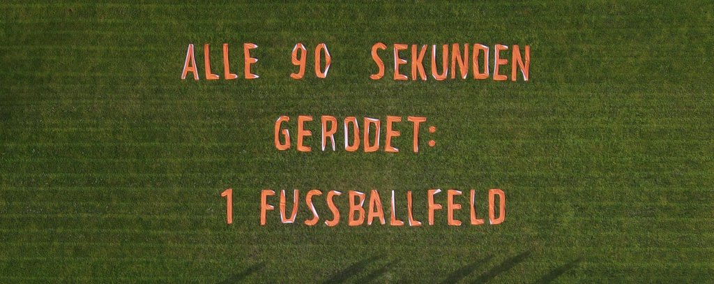 Protest gegen die Waldzerstörung für Importe in die EU - Installation im Berliner Hans-Zoschke-Stadion, 2.2.2022 (Foto: Nina Neuscheler / ROBIN WOOD) Luftaufnahme von einem Banner gegen Waldzerstörung,das auf einem Fußballfeld liegt