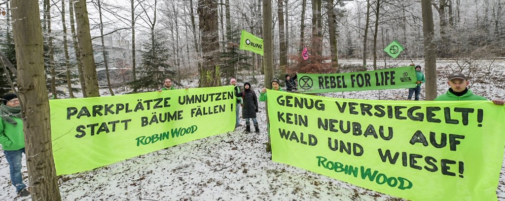 Umweltschützer*innen mit zwei Bannern vor Bäumen