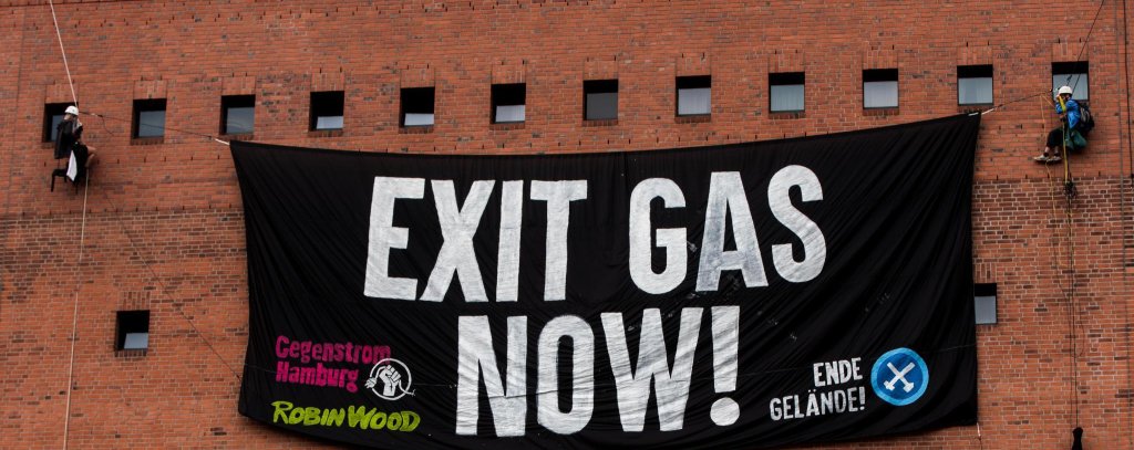 Gasausstieg jetzt! - Kletterprotest an der Hamburger Elbphilharmonie, 8.8.22 (Foto: Pay Numrich / ROBIN WOOD) Kletter*innen vor der Fassade der Elbphilharmonie mit einem Protestbanner. Aufschrift: Exit Gas Now!