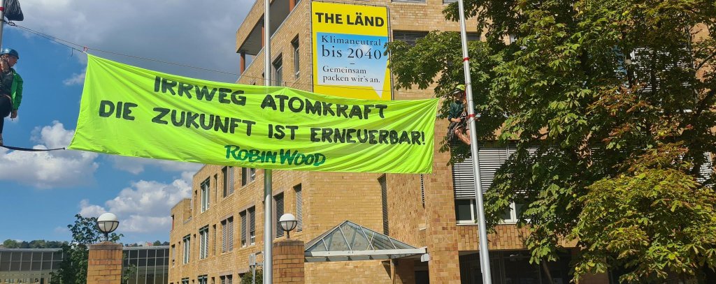Gelbes Protestbanner zwischen Fahenmasten vor dem Umweltministerium in Stuttgart