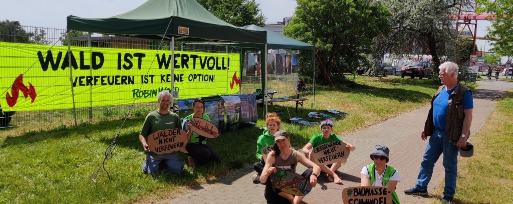 Wald ist wertvoll - Verfeuern ist keine Option! Protest vor dem Werk von Wismar Pellets, 22.05.2023 (Foto: ROBIN WOOD) Aktive sitzen mit Protestschildern auf dem Boden vor einem Pelletwerk