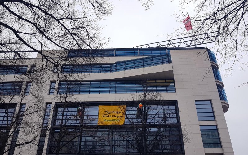 Zwei Kletter*innen haben sich mit einem Banner vor der Fassade des Willy-Brandt-Hauses in Berlin abgeseilt. Banner-Aufschrift: Flüge statt Züge! ROBIN WOOD