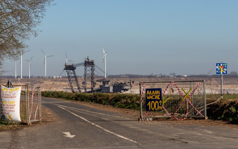Moritz Heck Bauzäune mit Protestplakat "Mahnwache 100 Meter", Bagger im Hintergrund