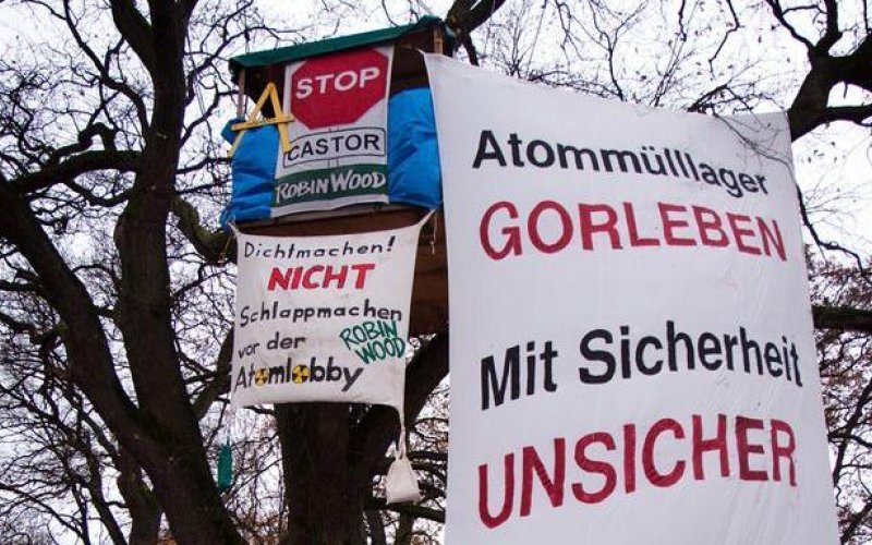 Baumhaus mit zahlreichen Bannern in einer großen Eiche. Auf einem Banner das bis zum Boden reicht steht "Atommülllager Gorleben - mit Sicherheit Unsicher - ROBIN WOOD"