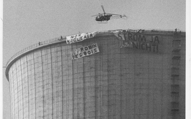 Schwarz-weißfoto: Aktivisten protestieren auf dem Kühlturm des AKW Cattenom. Dort entrollen sie in 165 Meter Höhe Transparente mit der Aufschrift „Strom ja – so nicht!“ und „Non au nucleaire!