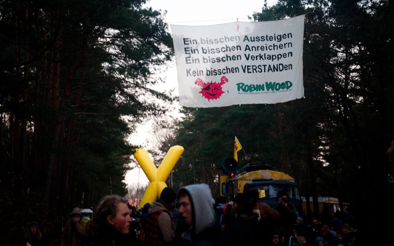 Aktivist*innen haben ein Banner über einer Demo gehängt. Darauf steht "Ein bisschen Aussteigen, Ein bisschen Anreichern, ein bisschen veklappen, kein bisschen VERSTANDen - ROBIN WOOD"