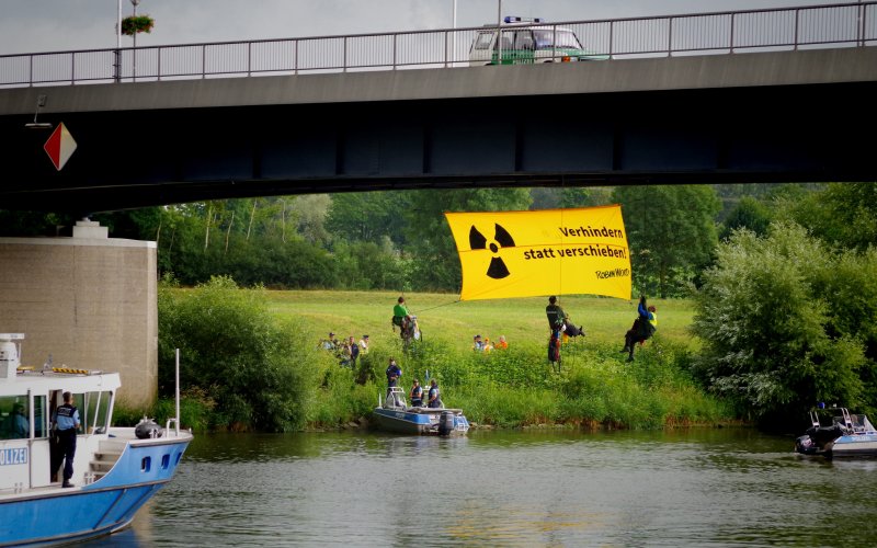 Aktivist*innen haben sich mit einem Banner von einer Brücke über dem Neckar abgeseilt. Auf dem gelben Banner steht; Verhindern statt verschieben - ROBIN WOOD