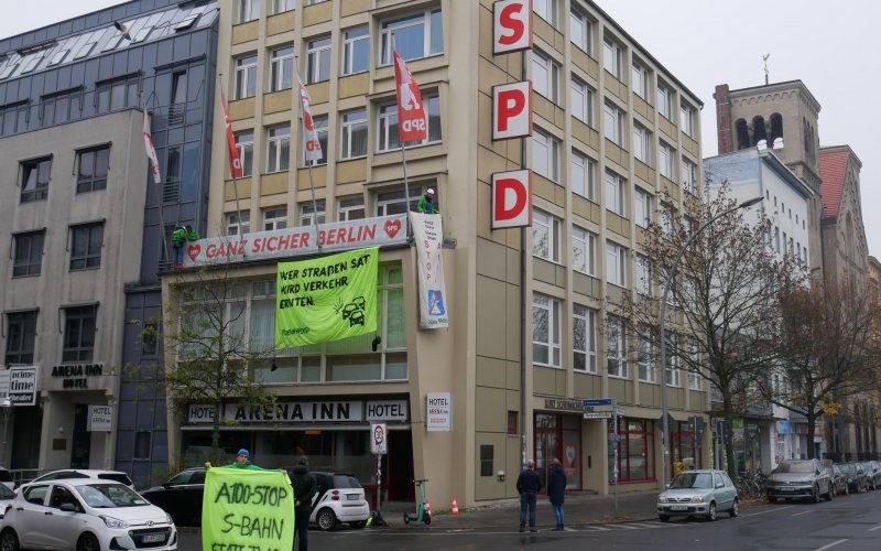 Fassade der Berliner SPD-Zentrale mit zwei Protestbannern. Am Boden steht ein Aktivist mit einem weitren Handbanner für einen Stopp des Weiterbaus der Stadtautobahn A100