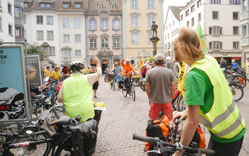 Radler*innen begrüßen weitere Radler*innen der Tour bei Ankunft auf einem Platz in Schaffhausen