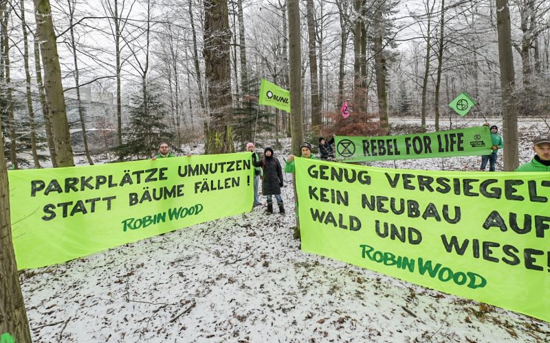 Umweltschützer*innen mit zwei Bannern vor Bäumen