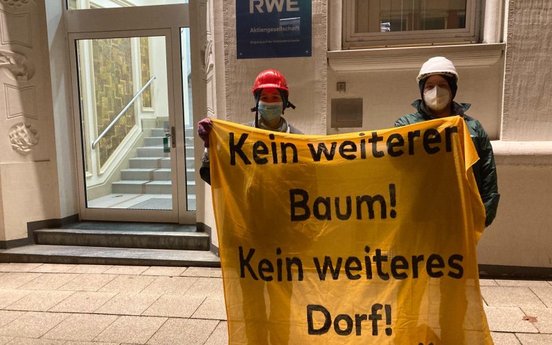 Zwei Aktivisten mit Banner am Boden vor der RWE-Zentrale