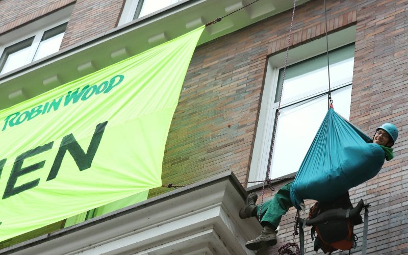 Ein Aktivist hängt in einer Hängematte neben dem Banner vor der RWE-Fassade