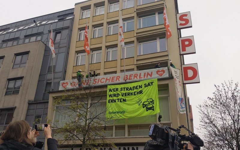 Kletter-Aktivist*innen haben ein Banner am Kurt-Schumacher-Haus der SPD in Berlin befestigt. Aufschrift: "Wer Straßen sät, wird Verkehr ernten. ROBIN WOOD"