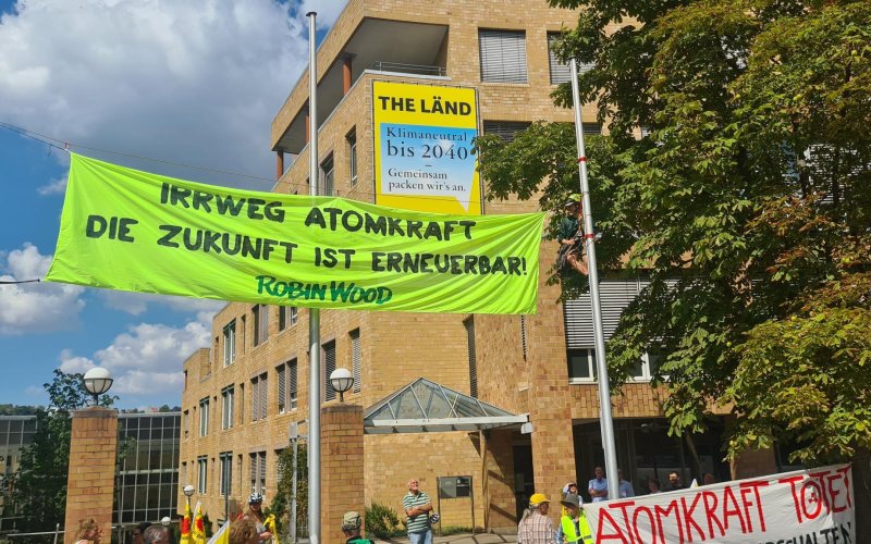 Gelbes Protestbanner zwischen Fahenmasten vor dem Umweltministerium in Stuttgart