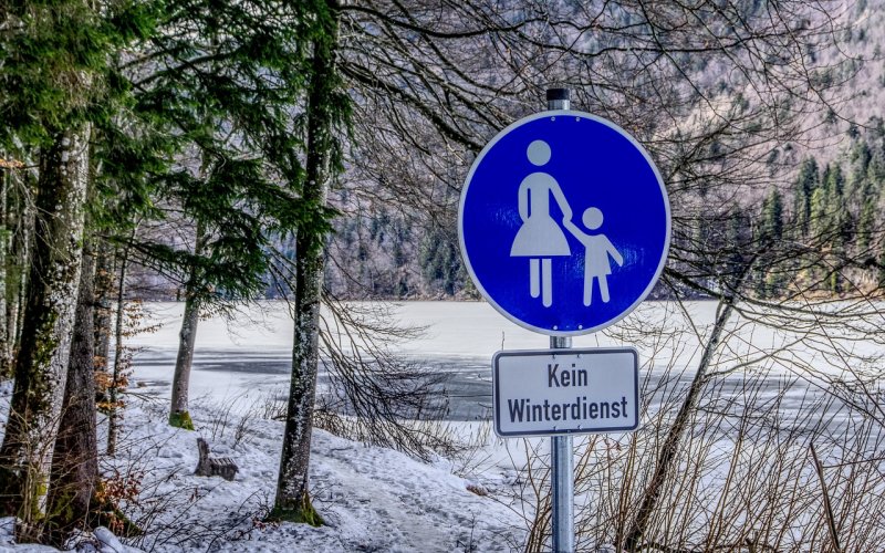 Gehwegzeichen "Kein Winterdienst" vor verschneiter Landschaft